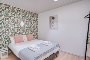 A bedroom with a floral wallpaper, a bed with pillows, a painting on the wall, and a wooden floor. - Wine Lodge - Two Bedroom Apartment, Sleeps 4 (Libourne)