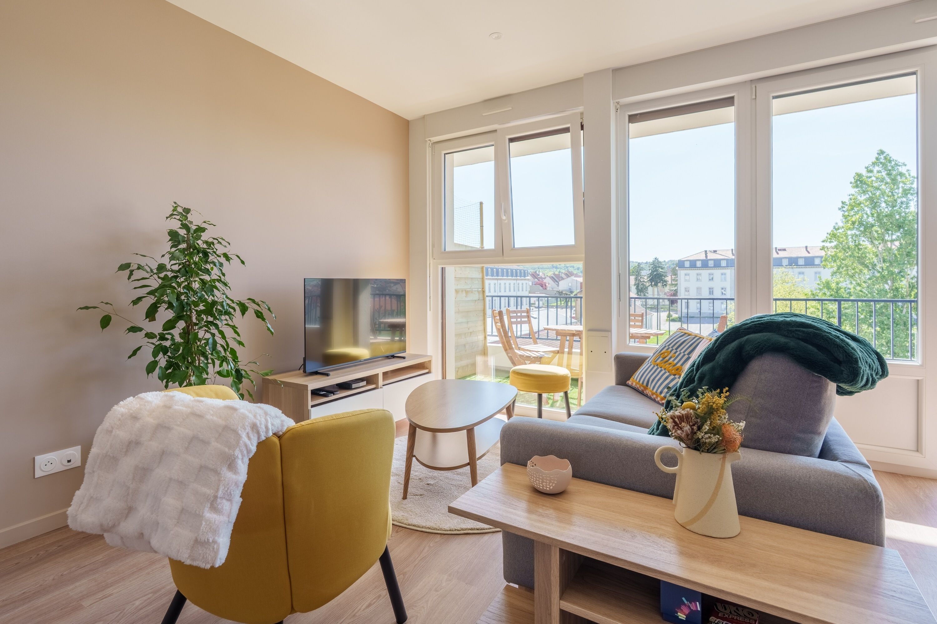A modern living room with a sofa, a TV, a dining table, and a large window.