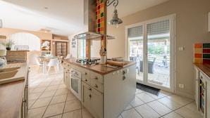 A modern kitchen with a central island, a dining area, and a view of the outdoors. - Rosie - Jolie maison avec terrasse et piscine (Le Verdon-sur-Mer)