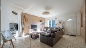 A living room with a sofa, TV, and a chair. - Rosie - Jolie maison avec terrasse et piscine (Le Verdon-sur-Mer)