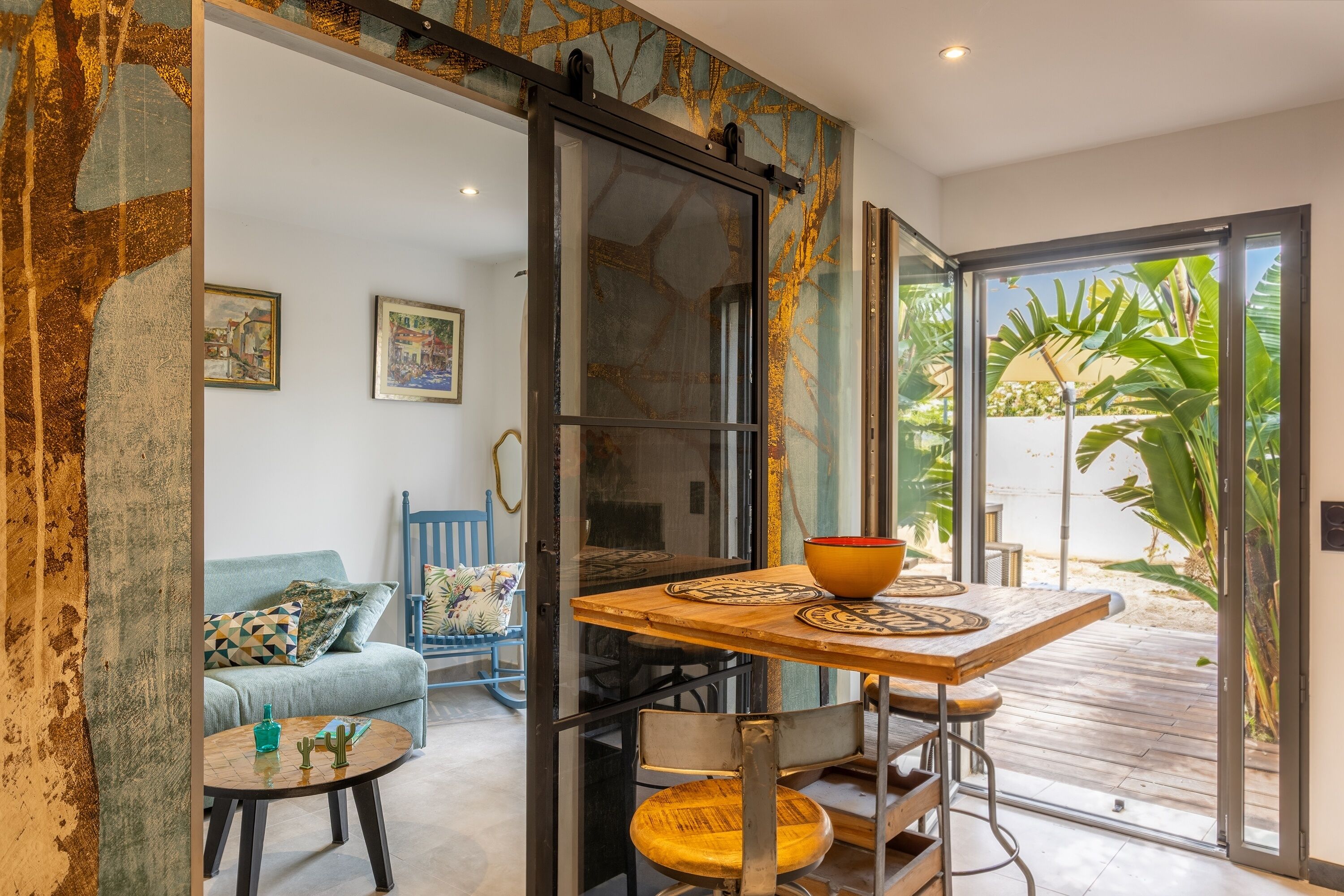 A room with a sliding glass door leading to a patio, a wooden table with a bowl, a blue sofa, and two framed pictures on the wall.
