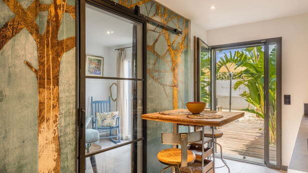 Ein modernes Interieur mit einer Schiebetür zu einer Terrasse, einem Holztisch mit Stühlen und Blick auf Grünflächen.
