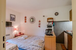Una stanza compatta con un letto, una scrivania piccola con un bollitore, uno specchio, una sveglia e una televisione su un supporto.