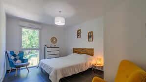 Ein Schlafzimmer mit Bett, Sessel, Nachttisch mit Lampe, Fenster und Wanduhr.