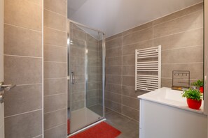 Ein modernes Badezimmer mit Duschkabine aus Glas, einem weißen Waschbecken und einer roten Fußmatte.