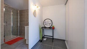 Ein modernes Badezimmer mit Duschkabine aus Glas, einer roten Fußmatte, einem wandmontierten Spiegel und einem kleinen Tisch mit Pflanze.