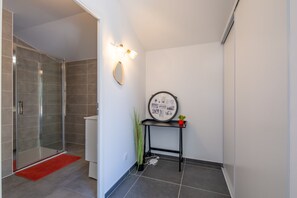 A modern bathroom with a glass shower enclosure, a red mat, a wall-mounted mirror, and a small table with a plant. - Oakline Azur - Bel appartement avec terrasse (Saint Raphael)