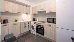 Eine moderne Küche mit Holzausstattung, einer Waschmaschine, einem Backofen, einer Mikrowelle und einem Kühlschrank.
