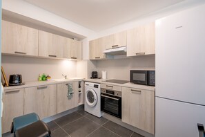 A modern kitchen with wooden cabinets, a washing machine, an oven, a microwave, and a refrigerator. - Oakline Azur - Bel appartement avec terrasse (Saint Raphael)