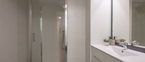 A modern bathroom with a glass shower enclosure, a white sink, and a large mirror.