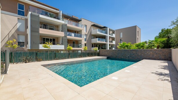 Ein modernes Apartmenthaus mit Schwimmbad, Balkonen und einer Steinmauer.
