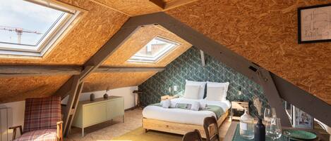 An attic bedroom with skylights, a bed, a chair, a table with glasses, and a map on the wall.