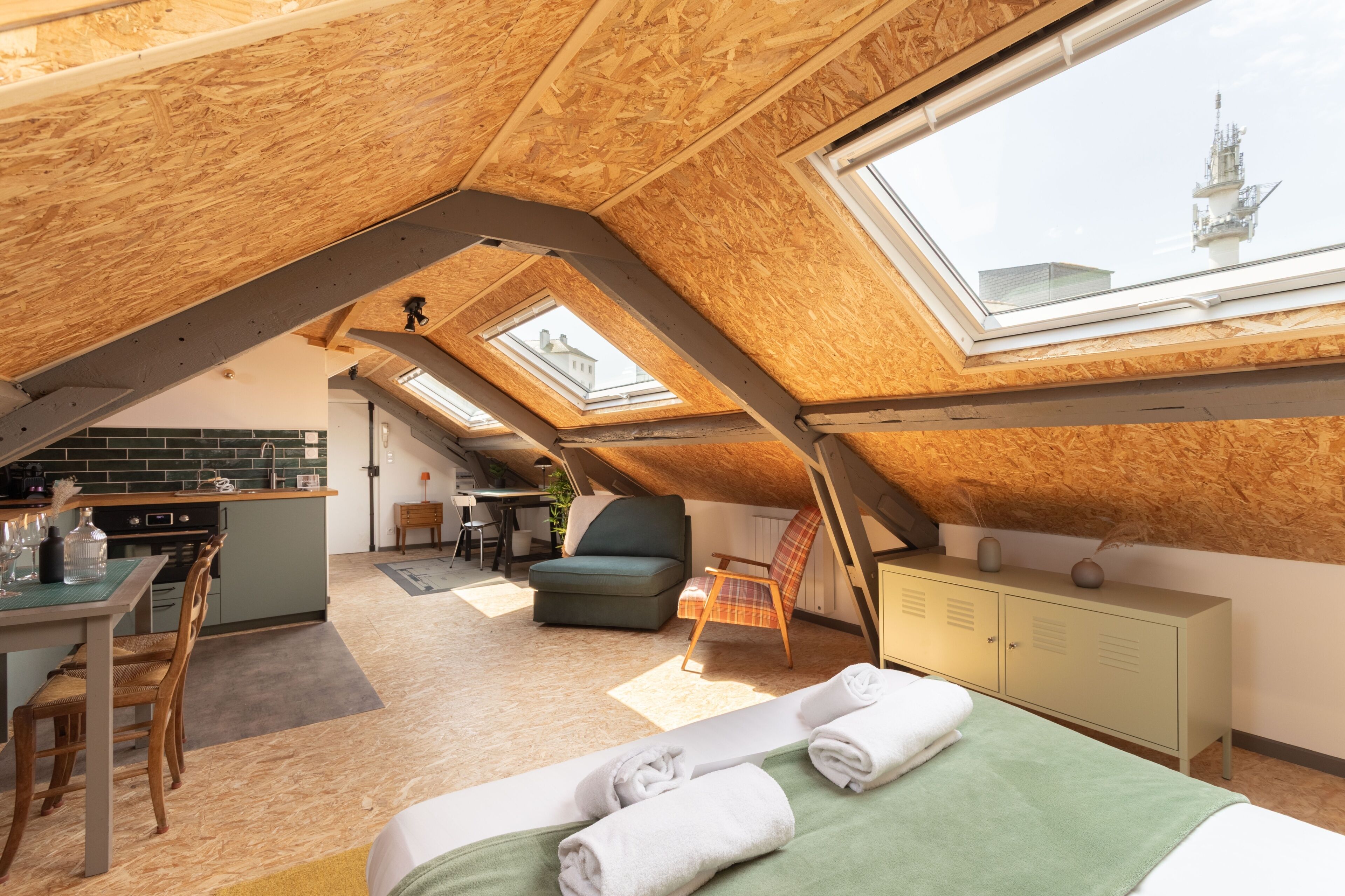 An attic bedroom with skylights, a bed, a desk, and a kitchenette.