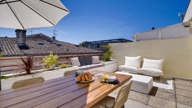 An outdoor patio with a wooden table, white cushions, and a white umbrella.