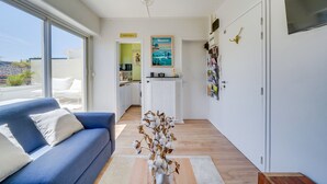 A modern living room with a blue sofa, a coffee table with a vase, and a view to a kitchen and dining area.