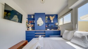 A bedroom with a bed, a bench, a TV, a dresser, and shelves with various items.