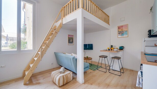 Una habitació amb un llit d'alt, un sofà, una petita cuina i una escala.