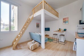 Une pièce comprenant un lit en mezzanine, un canapé, un petit coin cuisine et un escalier.
