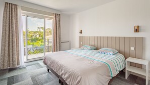 Une chambre dotée d’un grand lit, d’une table de chevet, d’une porte-fenêtre coulissante donnant sur un balcon et offrant une vue sur la verdure.