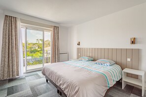 Ein Schlafzimmer mit einem großen Bett, einem Nachttisch, einer Glasschiebetür zu einem Balkon und Blick ins Grüne.