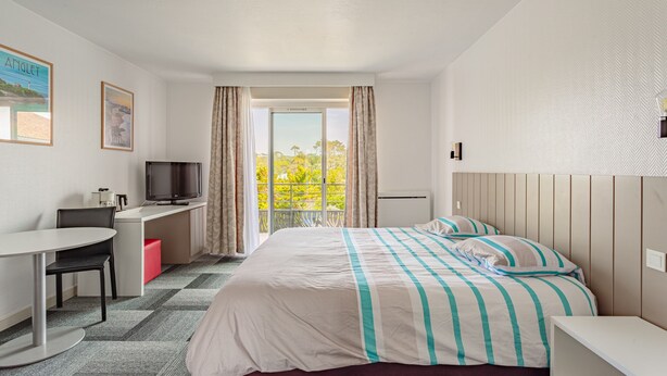 Une chambre d’hôtel avec un lit, un bureau, une télévision et une fenêtre avec des rideaux.