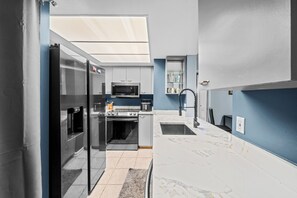 Eine kompakte Küche mit Mikrowelle, Backofen und Kühlschrank, einem kleinen Spülbecken und einem Fenster darüber.