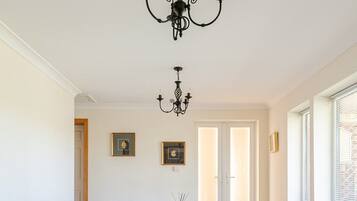 Comedor con una mesa blanca y cuatro sillas tapizadas, una lámpara de araña negra y cuadros en la pared.