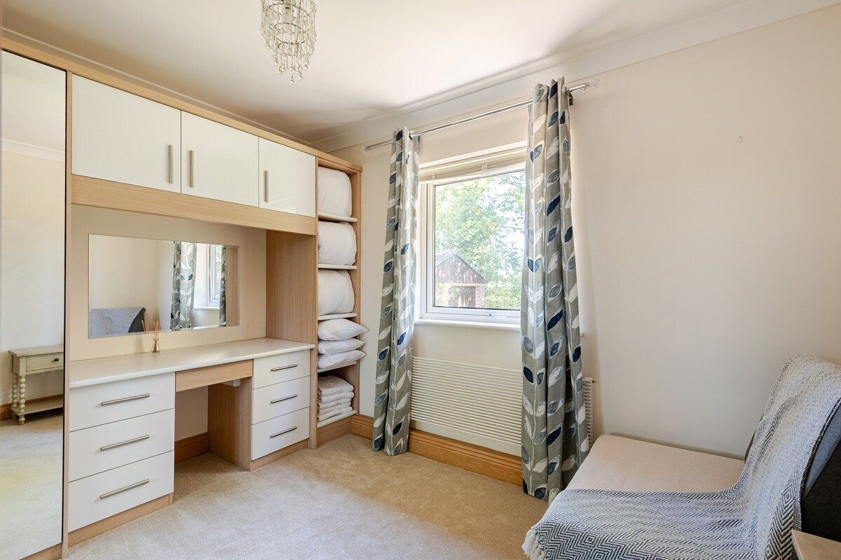 Un dormitorio con cama, escritorio, armario y ventana con cortinas.