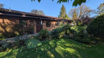 A brick house with a tiled roof, surrounded by a well-maintained garden with various plants and a lawn.