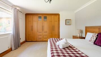 A bedroom with a large wardrobe, a bed with a checkered bedspread, a nightstand with a lamp, and a window with curtains.