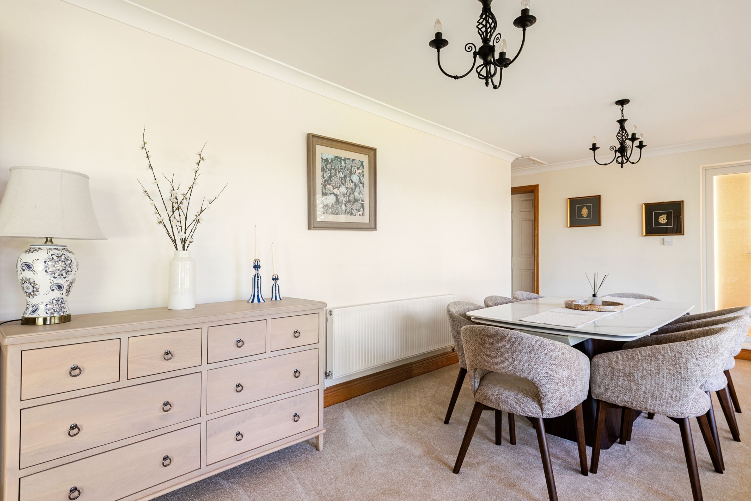A dining area with a table and chairs, a radiator, a cabinet with drawers, and wall-mounted picture frames.