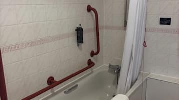 A bathroom with a bathtub, a shower, and a handrail.