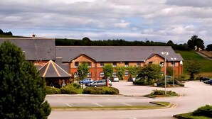 A hotel with a parking lot, a covered outdoor area, and a hilly landscape in the background. - Monifieth Farm Hotel (Dundee)
