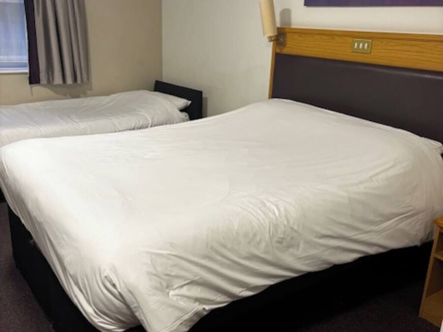 A hotel room with two beds, a painting on the wall, and a window with curtains.