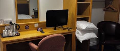 A hotel room with a bed, a desk with a computer, a chair, a mirror, a wardrobe, and a hanging coat rack.