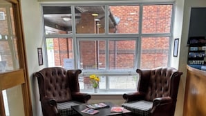 A room with two leather armchairs, a small table with magazines, a window with a view of a brick building, and a purple rug. - Monifieth Farm Hotel (Dundee)