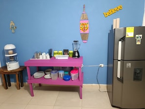 Une cuisine avec un plan de travail rose, un mixeur, un réfrigérateur et divers ustensiles de cuisine.