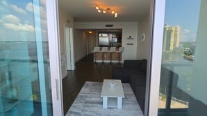 Una sala de estar moderna con comedor, cocina y vistas a un paisaje urbano a través de amplios ventanales.