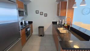Una cocina moderna con electrodomésticos de acero inoxidable, armarios de madera, piso de baldosas e iluminación colgante.