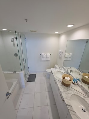 Een moderne badkamer met een glazen douchecabine, een marmeren wastafel en een grote spiegel.
