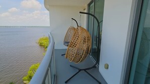 Un balcón con vista al agua, dos sillas de mimbre y una puerta de cristal.