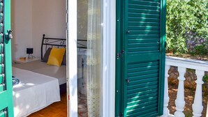 Ein Zimmer mit einem Bett, einem kleinen Tisch mit einer Lampe und einem Fenster mit grünen Fensterläden.