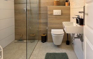 Un baño moderno con cabina de ducha de vidrio, inodoro, lavamanos y una pequeña alfombra en el suelo.