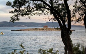 A tree in the foreground with a body of water and a distant island with a building. - Nice apartment in Novi Vinodolski with WiFi (Novi Vinodolski)
