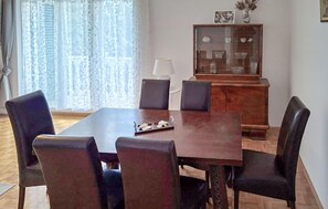 A dining room with a wooden table and four chairs, a cabinet with glass doors, and a window with sheer curtains. - Nice apartment in Novi Vinodolski with WiFi (Novi Vinodolski)