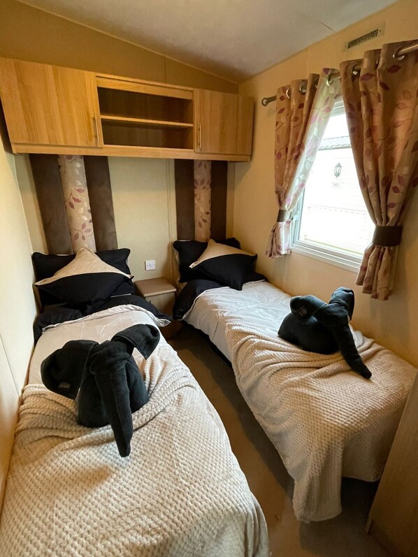 Une chambre de taille modeste, équipée de deux lits simples, d’une armoire en bois et d’une fenêtre avec des rideaux.