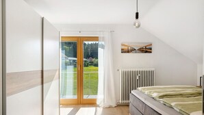 A bedroom with a bed, a radiator, a window with curtains, and a painting on the wall. - Dog-Friendly Holiday Apartment with 2 Balconies and Wi-Fi (Bräunlingen)