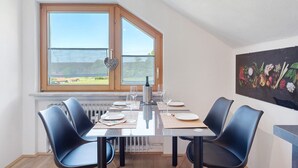 A dining area with a table set for four, a radiator below, and a window with a view of the outdoors. - Dog-Friendly Holiday Apartment with 2 Balconies and Wi-Fi (Bräunlingen)