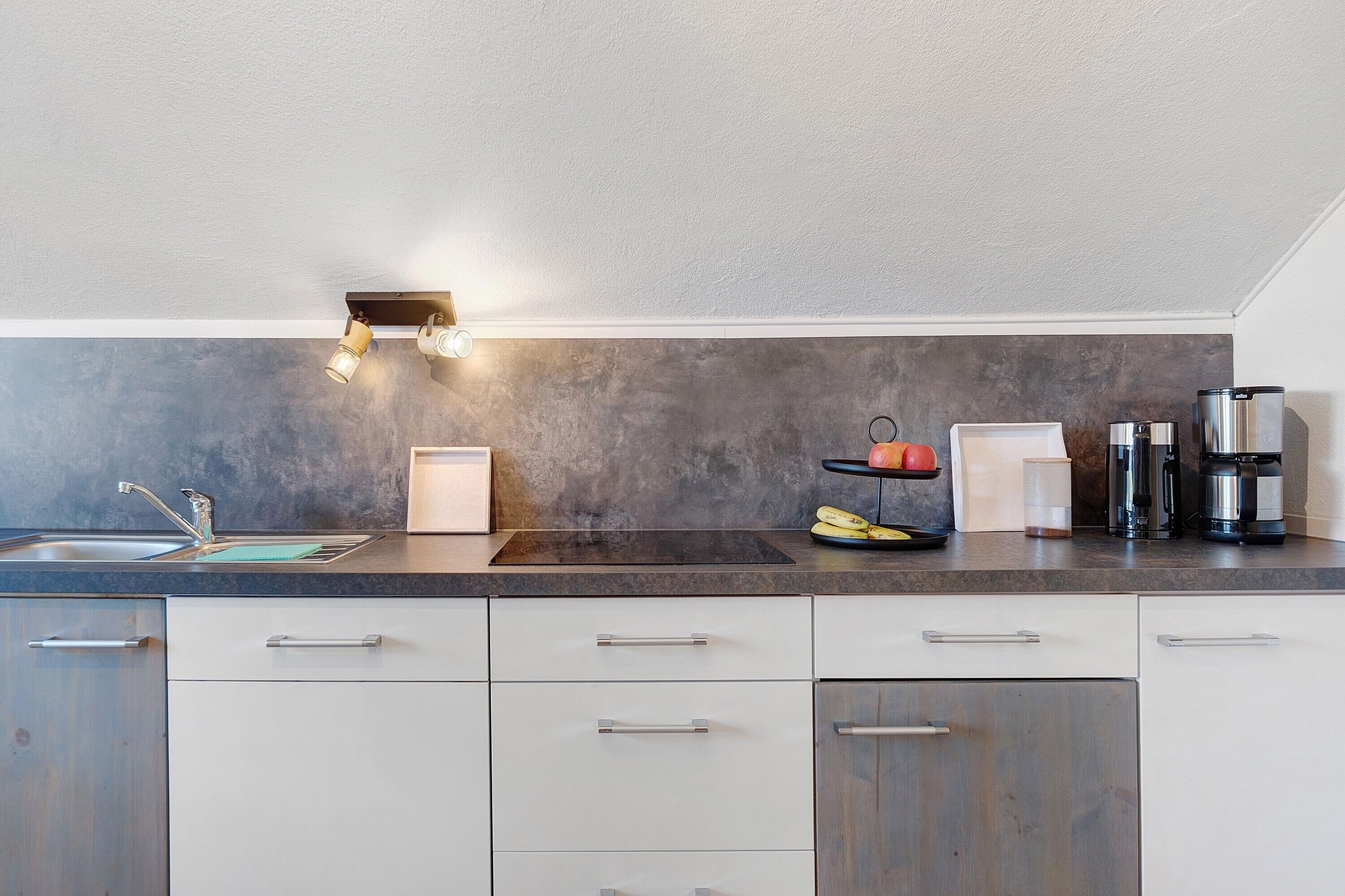 A modern kitchen with a dark countertop, white cabinets, a sink, and a coffee maker.