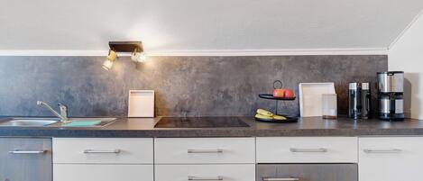 A modern kitchen with a dark countertop, white cabinets, a sink, and a coffee maker.